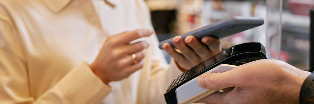 Website header shot of customer holding smartphone while making mobile payment using contactless payment terminal in retail environment, highlighting convenience and modern technology