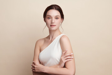Obraz premium A beautiful young woman with clean, fresh skin against a beige background. Skincare, facial treatment, cosmetology, beauty, and spa. An elegant portrait of an woman.