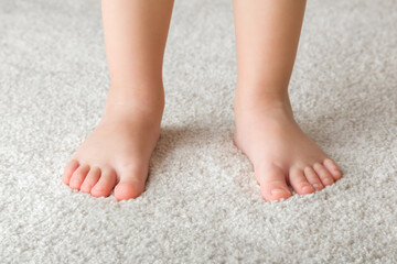 Cute baby feet standing on white soft home carpet. Front view. Barefoot closeup.