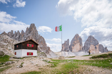 Hiker explores the Dolomites near a public refuge and Italian flag.