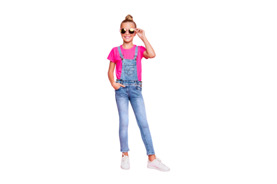 Full length body size photo of cute funny girl standing confidently in front of camera with hand in pocket wearing jeans overall footwear holding eyewear isolated over pastel pink color background