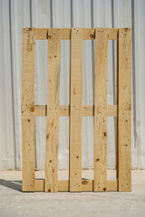 Wooden Pallet Standing Upright Against a Metal Fence in a Factory Garden in Sunlight