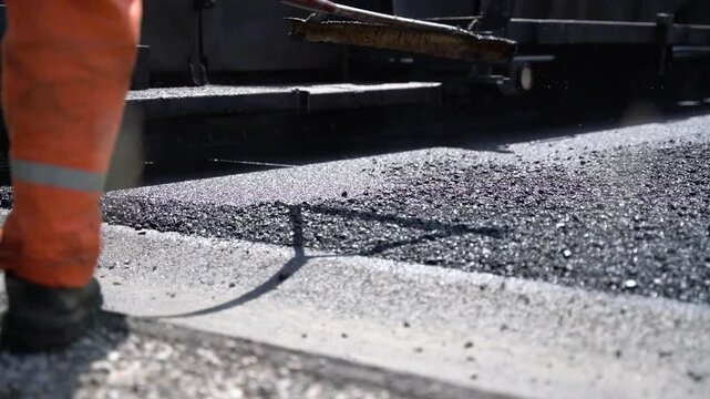 Construction worker spreading fresh asphalt with rake to ensure perfectly even finish on road construction site, close-up