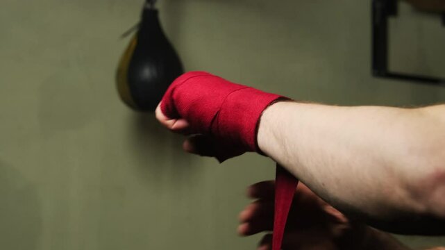 Man protects muscles and joints from damage with special fabric. Boxer wraps hands against speed bag preparing to begin exercise performance