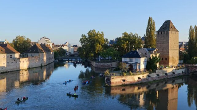 People canoeing on River Ill in city of Strasbourg at sunrise in Alsace, Grand Est, France. On the right medieval tower of Ponts Couverts - Covered Bridges.