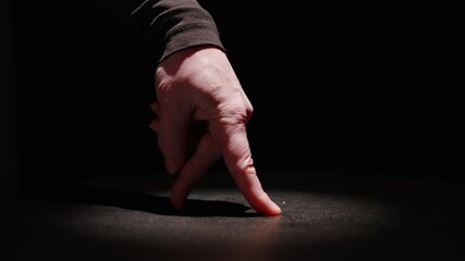 Moonwalk dance performed by fingers of man's hand in stage lighting on black background close-up.