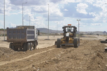 Obraz premium Dump Truck and Grader Operating Together on Dirt Road Project