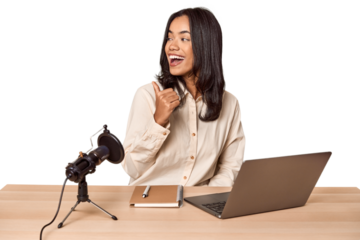 Woman records podcast with laptop points with thumb finger away, laughing and carefree.