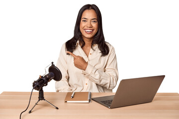 Woman records podcast with laptop smiling and pointing aside, showing something at blank space.