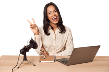 Woman records podcast with laptop joyful and carefree showing a peace symbol with fingers.