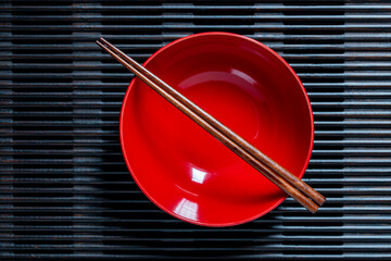 A pair of chopsticks lying across an empty red soup bowl on wooden striped tray, closeup, top view