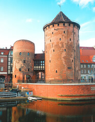 Picturesque view of the medieval Prison Tower and Torture Tower on the waterfront in Gdańsk, Poland. The scene features charming Hanseatic townhouses.