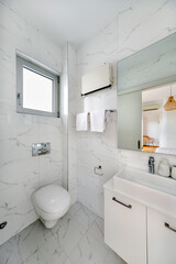 Contemporary bathroom with wall-mounted toilet, sleek white vanity, large mirror, and marble wall tiles. Clean design with modern fixtures and built-in heater for comfort.