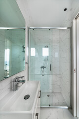 Obraz premium Modern bathroom interior in white tones, walk-in shower with glass partition and sliding door, white sink with mirror above, marble tiles, clean elegant design, bright minimalist space.