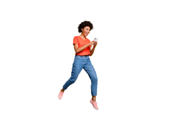 Full length photo of positive cheerful funny curly brown hair girl use smartphone read post blogs in social network jump wear red t-shirt denim jeans isolated over yellow color background