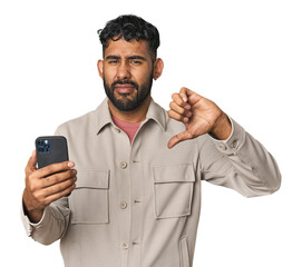 Hispanic male with mobile phone in studio showing a dislike gesture, thumbs down. Disagreement...