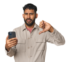 Hispanic male with mobile phone in studio showing a dislike gesture, thumbs down. Disagreement concept.