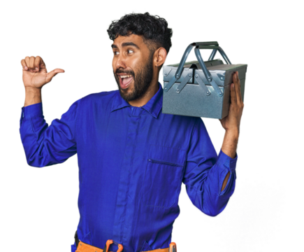 Hispanic worker with toolbox in studio points with thumb finger away, laughing and carefree. - Powered by Adobe