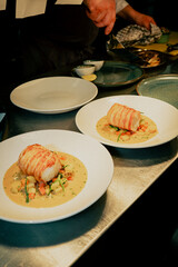 Two plates of food with a white sauce and vegetables on top. The plates are on a table and a person is standing behind them