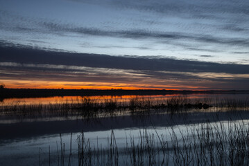 Colorful sunset over a calm lake with dramatic clouds and reflections on the water, creating a peaceful and scenic landscape view.