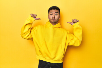 Bold Asian man in yellow hoodie on yellow studio feels proud and self confident, example to follow.