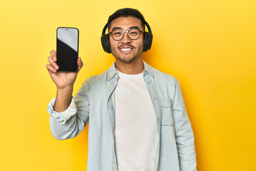 Asian man making a playlist on his phone while listening to music, on yellow background.