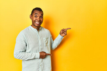 African American man in blue shirt, yellow studio, shocked pointing with index fingers to a copy...