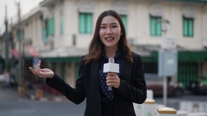 asian woman reporter presenting with microphone in front of old city architecture