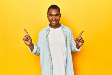 African American man in blue shirt, yellow studio, pointing to different copy spaces, choosing one...