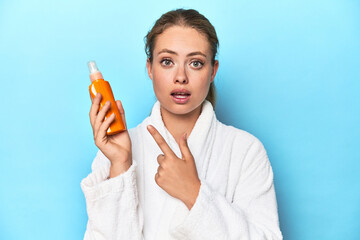 Fototapeta premium Blonde in bathrobe with sunscreen cream in studio pointing to the side