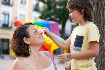 Child painting rainbow on mother's face at pride parade