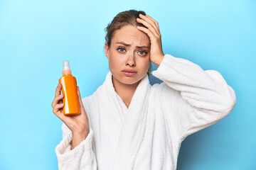 Blonde in bathrobe with sunscreen cream in studio being shocked, she has remembered important...