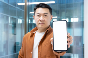 An Asian businessman holding out a smartphone with a blank screen, ideal for showcasing apps or...