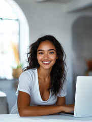 Naklejka premium Smiling young woman sitting at a table working on a laptop in a cozy indoor setting