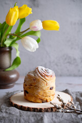 Easter Bread or Kulich with raisins. Easter yeast twisted cake Cruffin, painted eggs and tulip flowers on a stone background. Easter food.