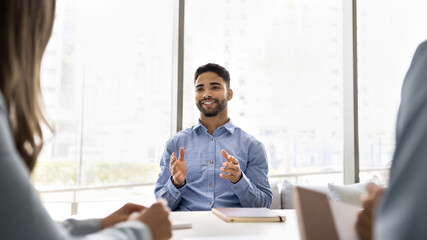 Confident speaker. Happy smiling young businessman expert consult workmates at boardroom desk. Professional specialist candidate for vacant place present himself to hr managers team on job interview