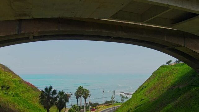 Push in drone shot under Eduardo Villena Rey Bridge and Pacific Ocean during the day in Malecon de Miraflores in the coast of Lima, Peru