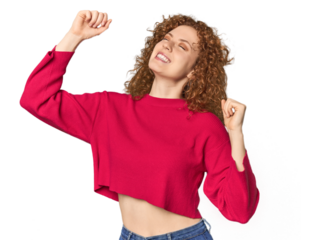 Young Caucasian redhead woman celebrating a special day, jumps and raise arms with energy.