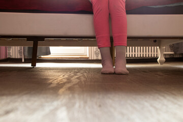Legs of a little girl sitting on a bed at home in her bedroom in socks and pajamas, baby's legs