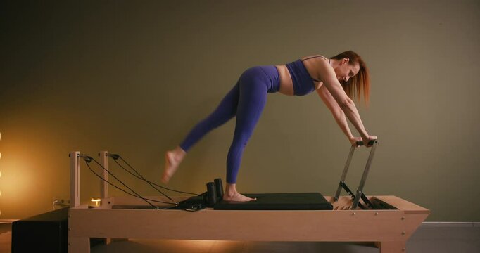 Woman doing pilates exercise on Pilates Reformer for the chest and back muscles, focusing on flexibility, strength, and control with determination