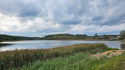  Photo of lake in the small village in Belarus. Dark heavy clouds above the loch. Green grass
