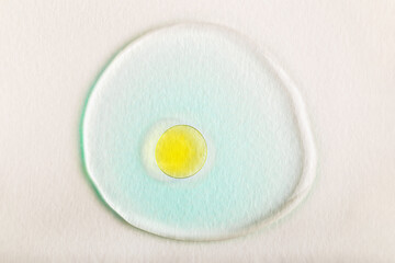 Close-up of yellow oil droplet in center of translucent blue serum layer on white background. Concept of skincare, wellness or product texture. Yellow drop in blue serum
