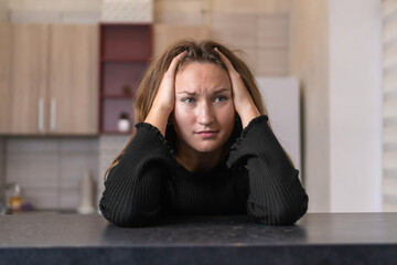 Exhausted woman suffering from headache or chronic migraine, sitting at kitchen table and touching...