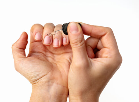 Close-up of female hand applying cuticle oil on natural nails using oil dropper.
