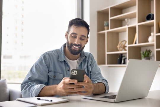 Communication and multitasking. Smiling young man remote worker student type text message on smartphone distracted from notebook use digital devices in home office to stay connected during work study - Powered by Adobe