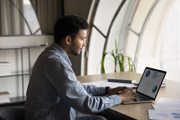 Busy manager analyzes dynamic market trends using AI application working on laptop, CEO navigates e-commerce platform, tracks financial flow, and strategizes for future growth. View over the shoulder