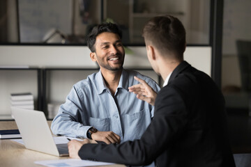 Authentic laughing Indian CEO business man listens to colleague. 2 managers speaking having candid discussion in the corporate boardroom. Two happy professionals collaborate and share ideas in office