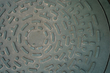 Manhole cover with intricate design on city street during daylight hours