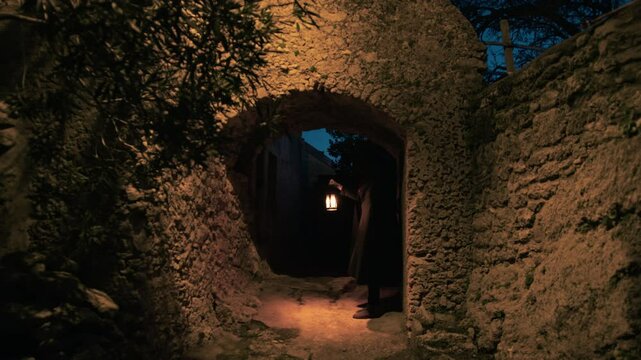 man in cloak waits under stone porch