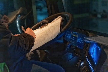 Driver is checking work papers in the cabin night lighting after the trip is over All potential trademarks are  removed. Horizontally.